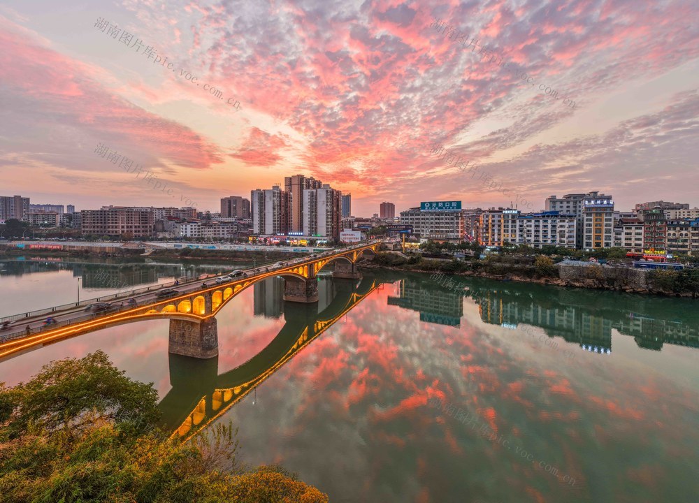 2025 年 12 月 11 日，湖南省永州市道县城区晚霞如画，错落楼宇、跨河桥梁与潋滟波光相映，构成一幅水天一色的生态美景。蒋克青摄影