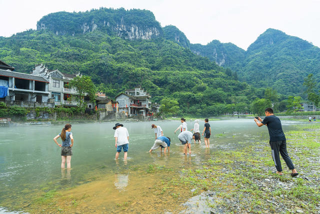 吉首市矮寨镇坪朗村，青山绿水环抱，河面薄雾缭绕，村民在石渡行走，苗寨宛如仙境